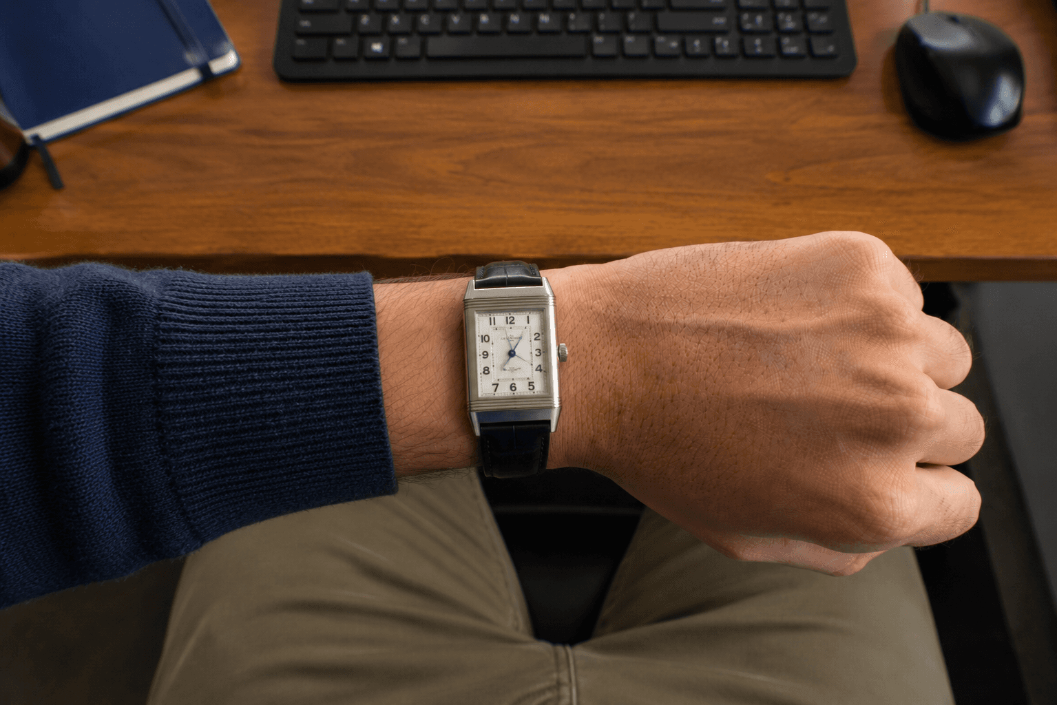 Rectangular dress watch on a wrist at a wooden desk